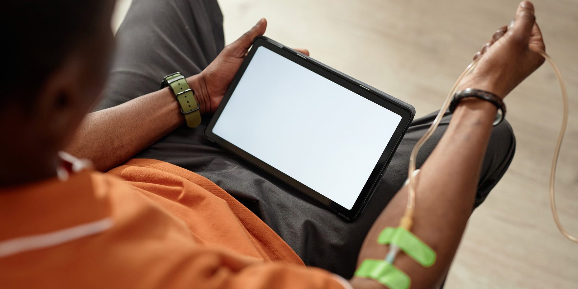 Black Man Using Tablet During IV Therapy. Top view closeup of unrecognizable African American man using digital tablet with white screen during IV therapy procedure in clinic